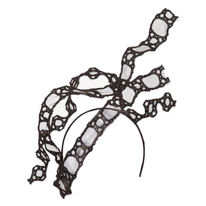 A black Piñatex headpiece on a narrow headband. It consists of three strands of Piñatex lasercut in a lacework pattern. They are in an asymmetric formation rippling from low on the right hand side as it would be worn, up into the air on the wearer's left..