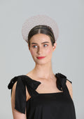 Woman wearing a black dress with bow details and a decorative dusky pink crown wire lace headpiece against a gray background